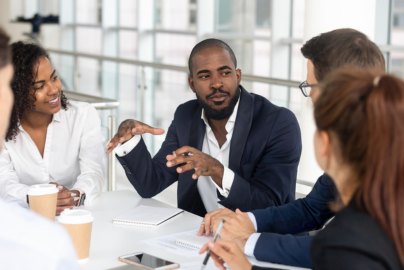 A group dressed in business casual clothes in conversation at a table in a bright room.
