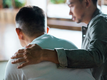 man with his arm around another man to comfort him