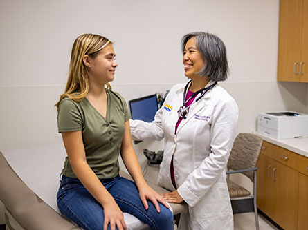 teenage girl sitting on a clinic table in a room with a female health care provider