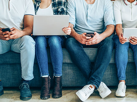 people sitting together on a couch all on mobile devices or laptops
